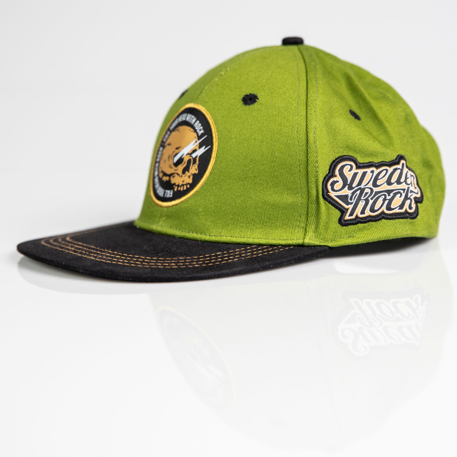 Keps Army/Black w patch är en grön och svart keps med böjd skärm, ett runt gult och svart frontmärke och en "Sweden Rock"-logotyp på sidan, mot en vit bakgrund.