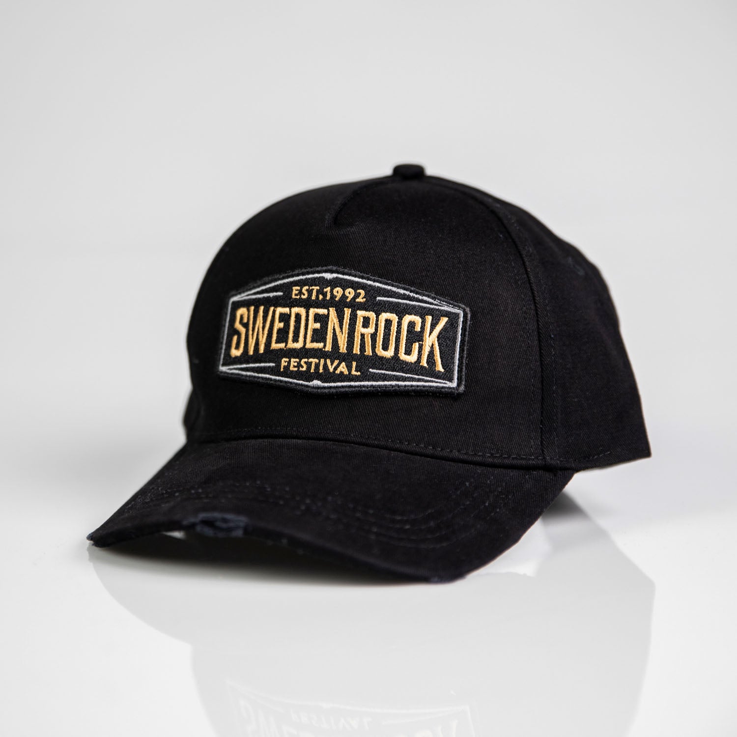 Keps Black & Gold - en svart bomullskeps med böjd skärm och "Sweden Rock Festival Est. 1992" broderat i beige och vitt på frontpanelen, visas på en vit yta.
