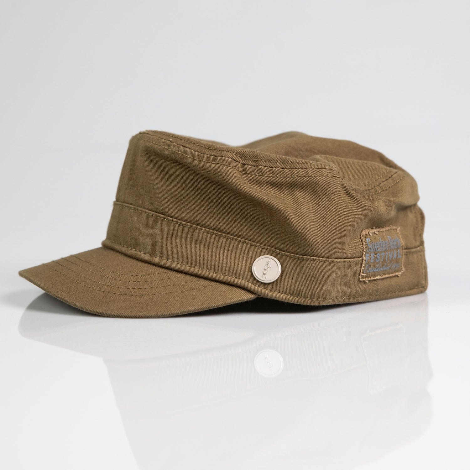 Army" är en brun keps i militär stil med platt topp, kort skärm, rund metallknapp och fransig tyglapp på sidan, tillverkad av bomull och visad på en vit reflekterande yta.