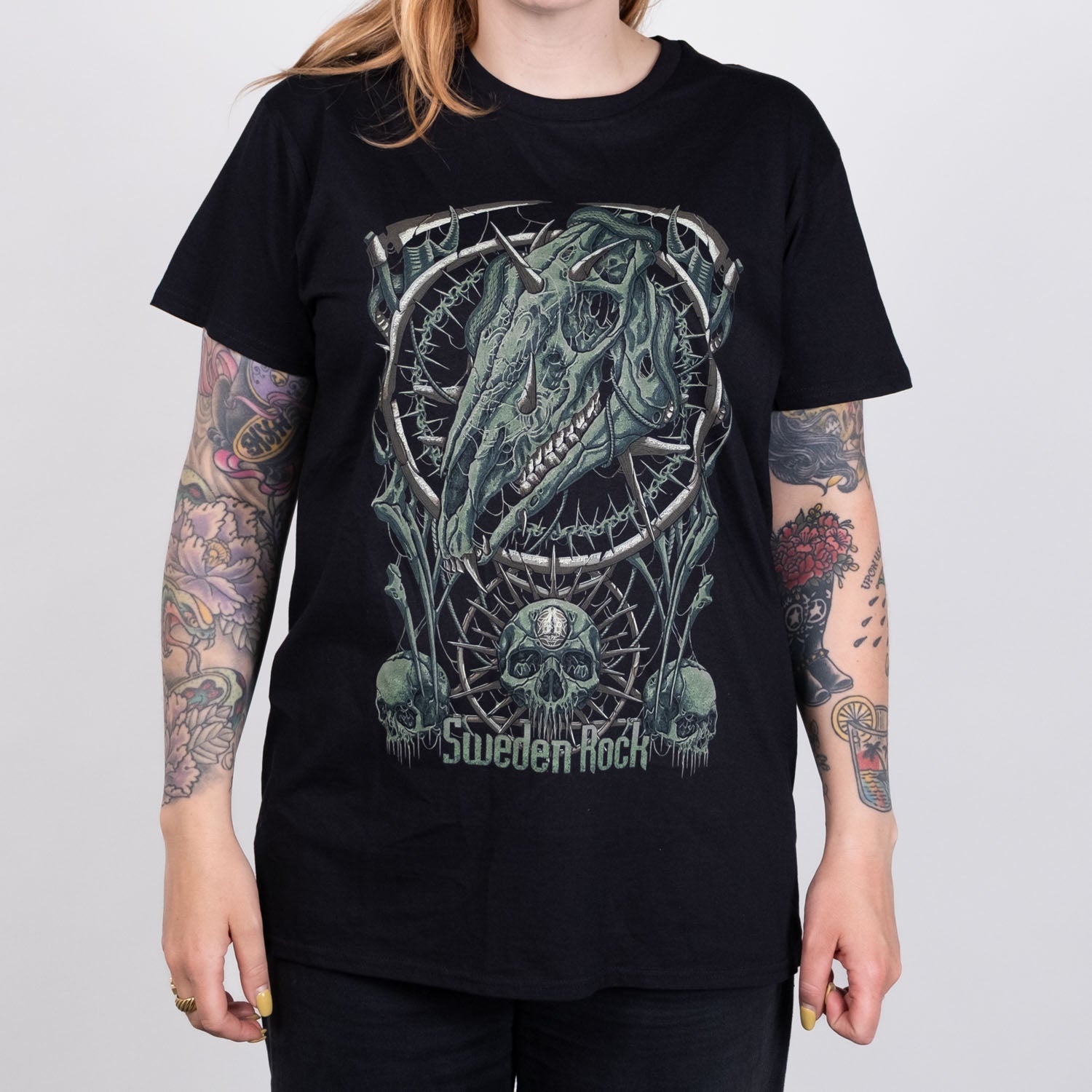 En person med tatuerade armar bär den svarta unisex-T-shirten Limited 1 med liemannen, dödskallar, taggtråd och texten "Sweden Rock" på framsidan. Tillverkad av ekologisk bomull. Bakgrunden är enfärgad ljusgrå.