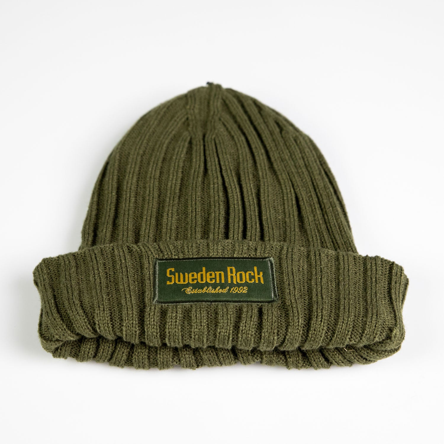 Beanie Ribbstickad är en grön ribbstickad mössa i mjuk akryl med vikt brätte och en frontpatch där det står "Sweden Rock Established 1992" i gult. Mössan visas platt på en vit bakgrund.