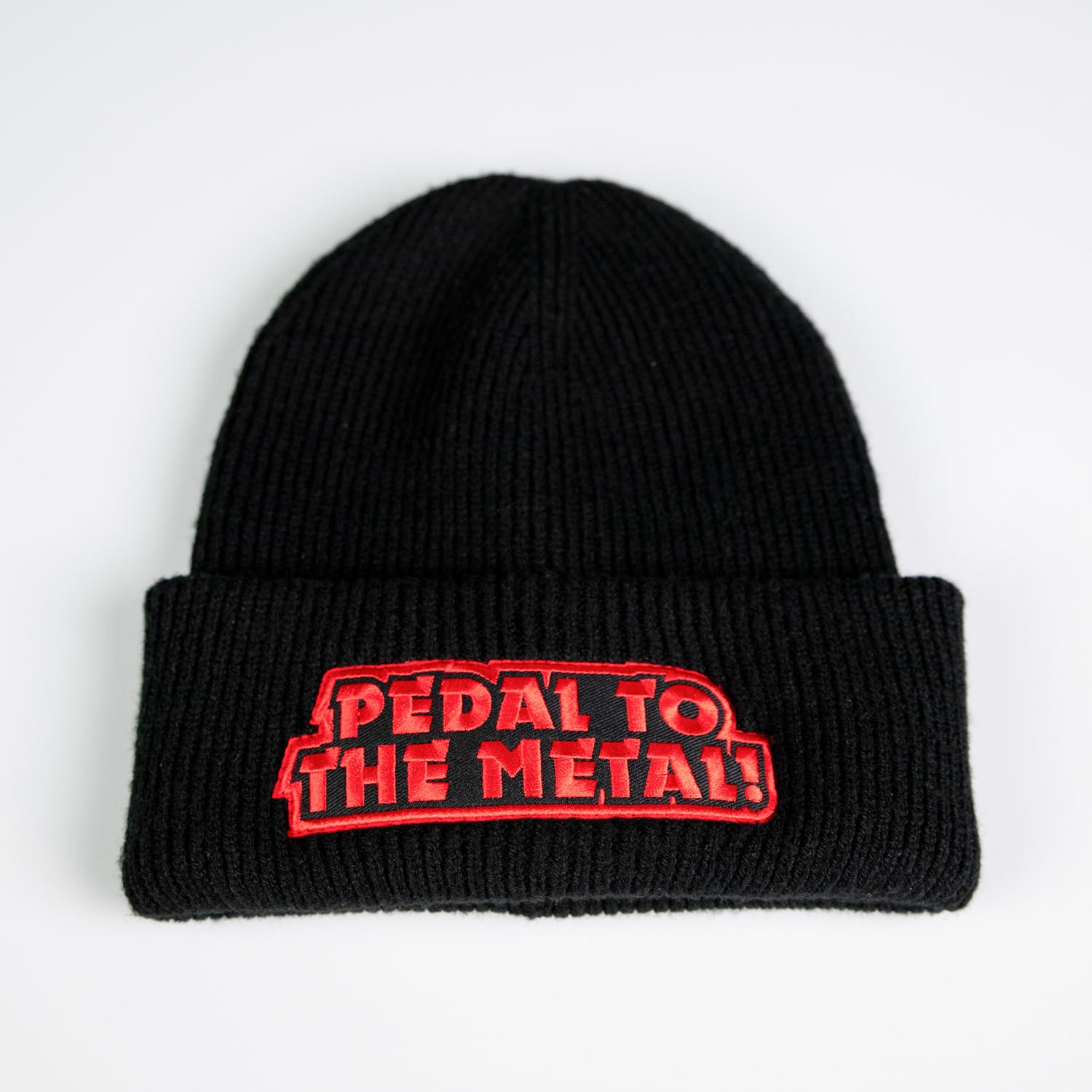 Mössa Pedal to the Metal är en svart stickad mössa med en mjuk polyesterstruktur, vikt brätte och en rödvit patch med texten "PEDAL TO THE METAL!" i versaler.
