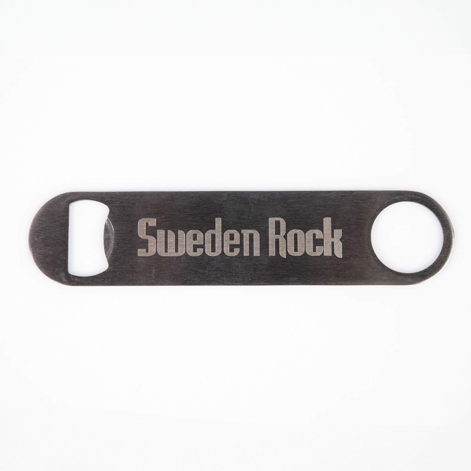 Kapsylöppnare är en flasköppnare i platt metall med Sweden Rock-loggan ingraverad, med ett runt hål i ena änden och en öppning för flasköppning i den andra, mot en vit bakgrund.