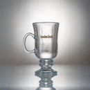 Ett 2-pack klara irländska kaffe-glasmuggar, var och en med handtag, kort piedestalbas och guldfärgad "Sweden Rock"-text på sidan, mot en enfärgad bakgrund.