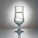 Ett klart ölglas från Ölglas 2-pack, med Sweden Rock i guld och svart på sidan, visas på en reflekterande yta mot en gråtonad bakgrund.