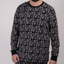 En man står mot en enfärgad bakgrund, klädd i "Pyjamas Kids" - en svart långärmad bomullströja med grå cirkelformade grafiska mönster och handsymboler. Hans ansikte är delvis utanför bild.