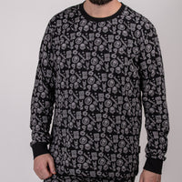 En man står mot en enfärgad bakgrund, klädd i "Pyjamas Kids" - en svart långärmad bomullströja med grå cirkelformade grafiska mönster och handsymboler. Hans ansikte är delvis utanför bild.