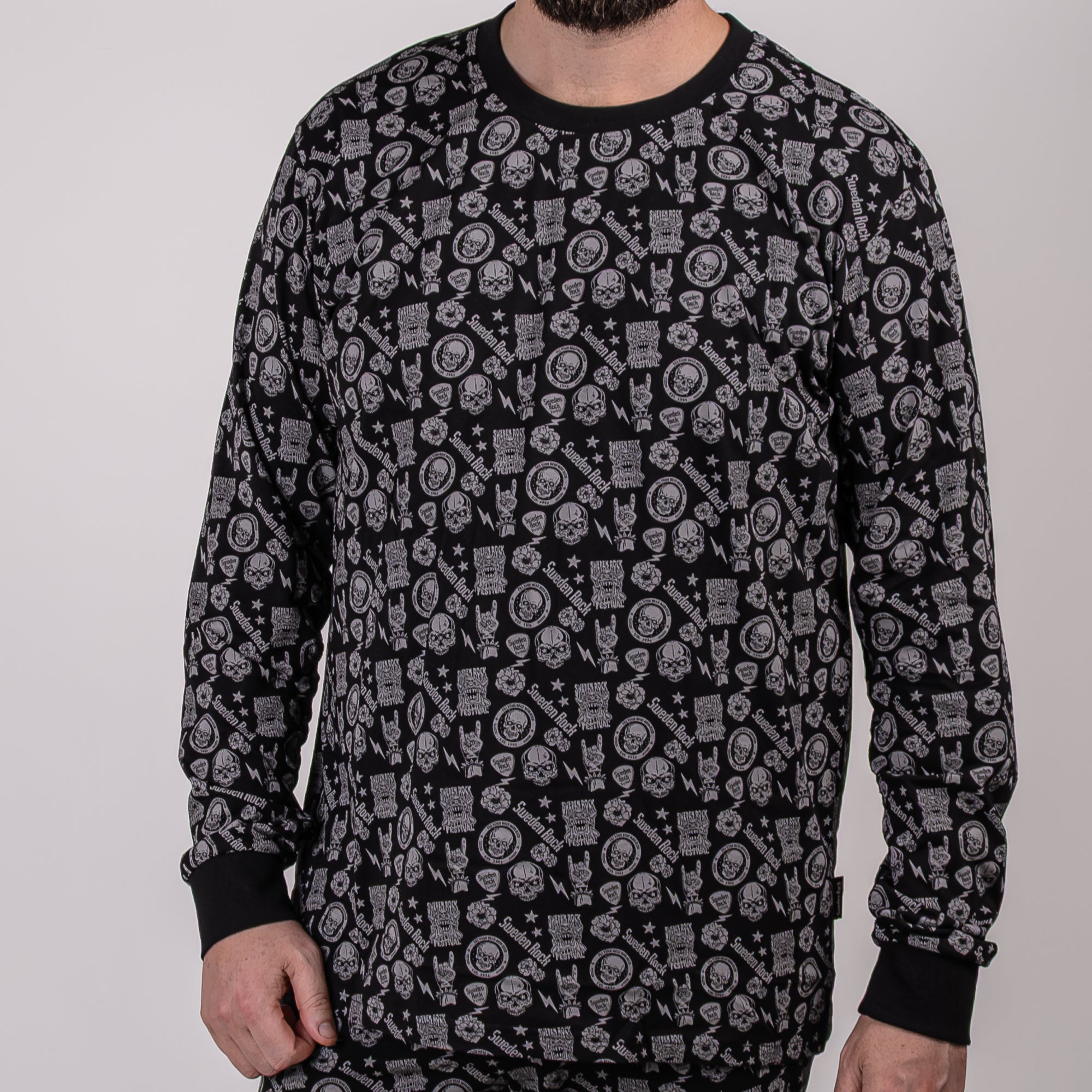 En man står mot en enfärgad bakgrund, klädd i "Pyjamas Kids" - en svart långärmad bomullströja med grå cirkelformade grafiska mönster och handsymboler. Hans ansikte är delvis utanför bild.