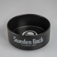 A svart keramikskål kallad Skål med "Sweden Rock Established 1992" i vitt på sidan. Insidan har en dödskallegrafik och texten "BLOW YOUR HEAD WITH ROCK" - den perfekta skålen för rockfans!.
