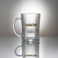 Ölsejdel 2-pack innehåller muggar i klarglas med handtag och "Sweden Rock" tryckt i guld och svart på sidan, som visas på en reflekterande yta med en neutral gradientbakgrund.