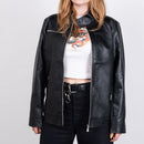 En person står mot en enfärgad bakgrund iklädd Läderjacka (svart PU-läderjacka), en vit crop top med drakmotiv, svarta byxor och ett svart bälte med metallklämma; ansiktet är delvis utanför bild.